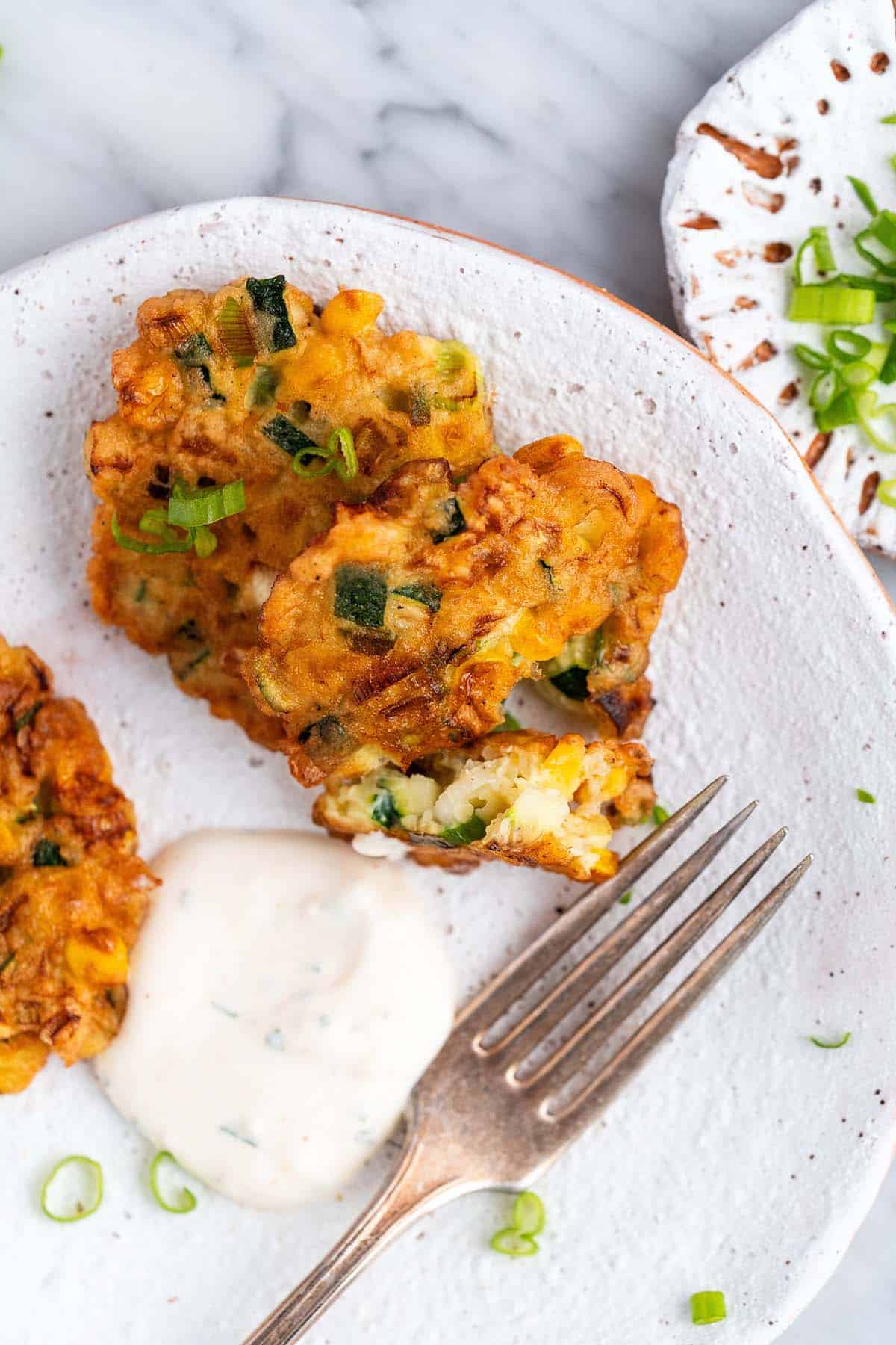 crispy veg fritters with creamy garlic sauce on plate with one fritter bitten to show inside