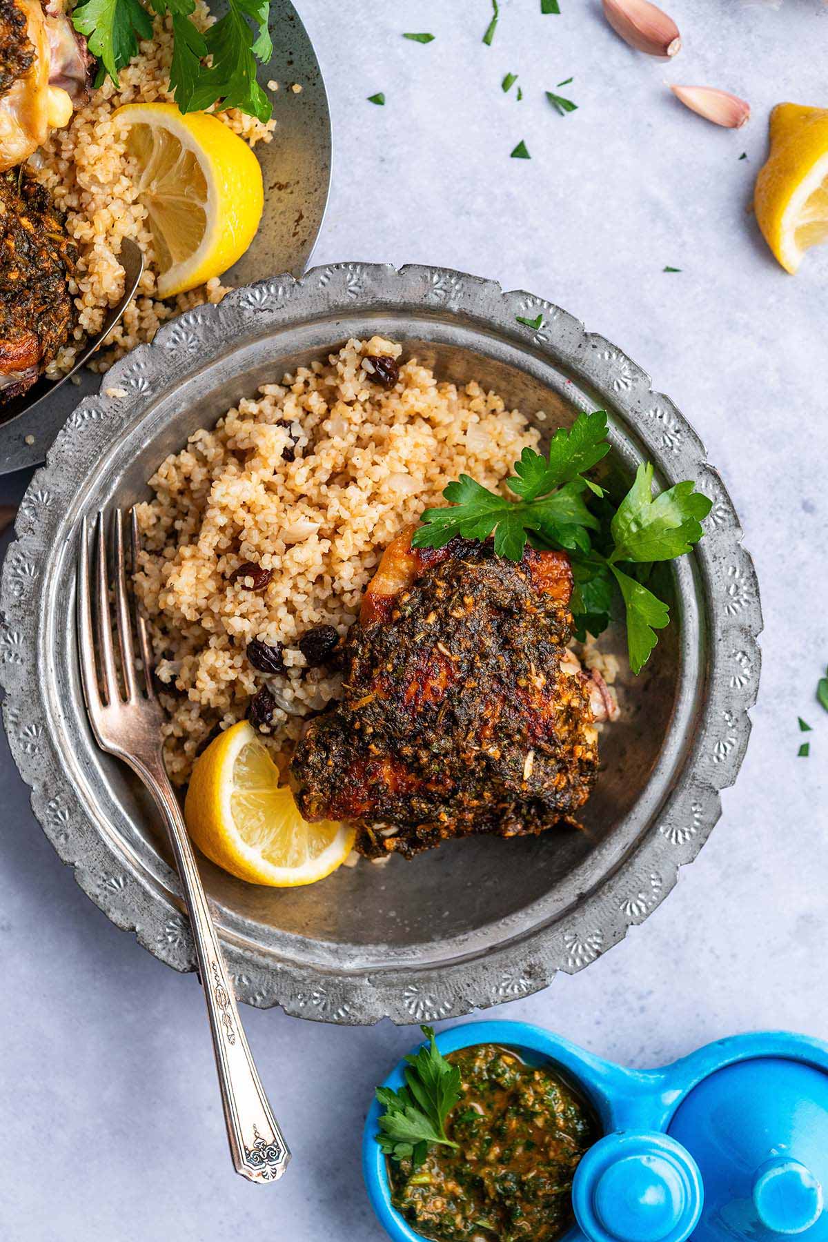Chermoula chicken recipe plated with bulgur pilaf side dish and Chermoula sauce in tagine condiment dish