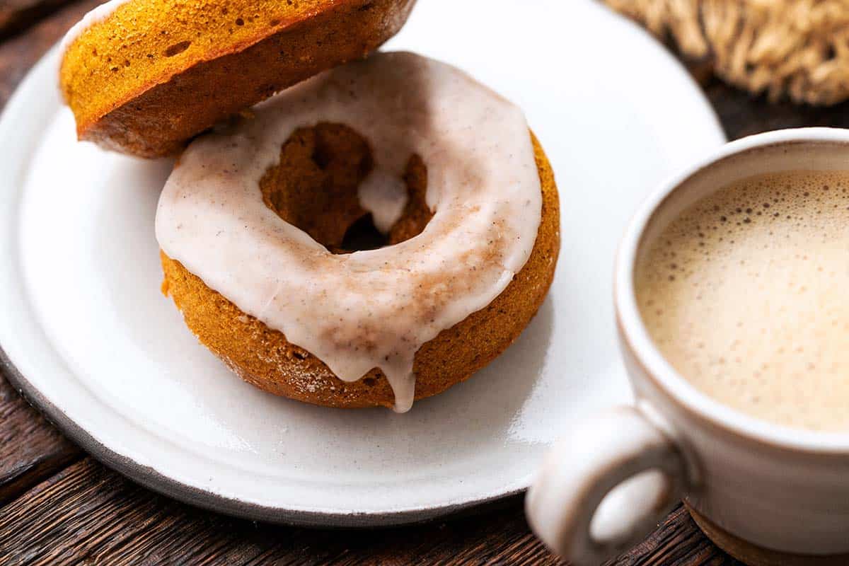 2 pumpkin spice donuts on white plate with espresso in front