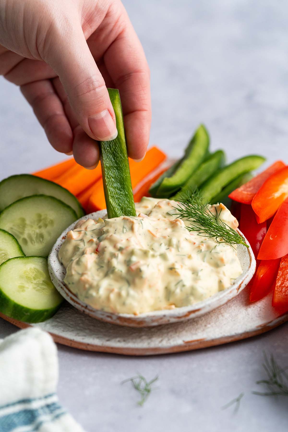 hand dipping green bell pepper strip into garden vegetable cream cheese dip