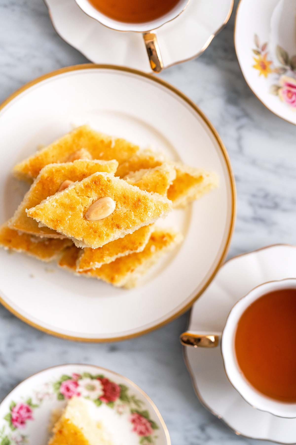 top view of middle eastern semolina cake on plate with cups of tea around