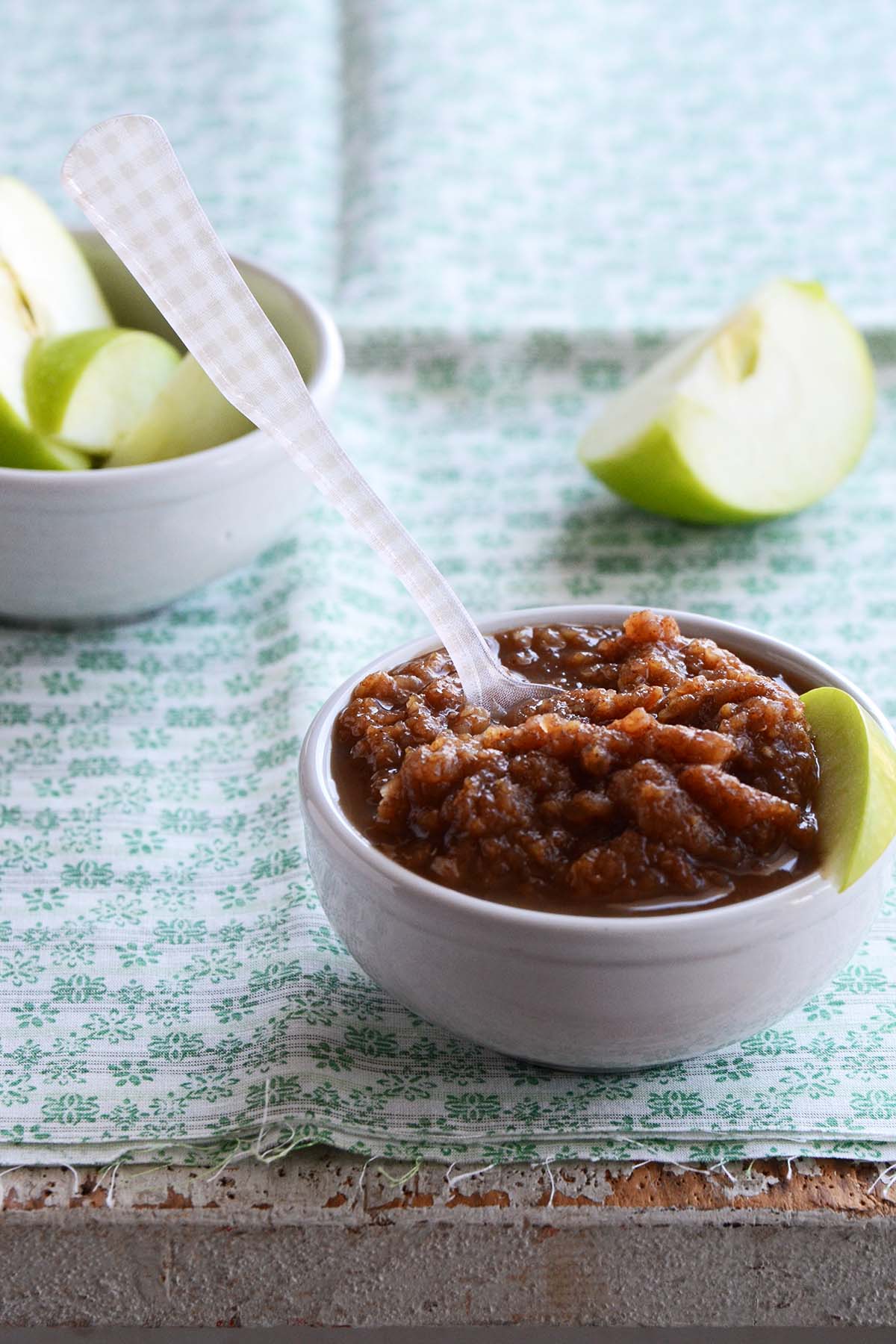 front view of applesauce made from zucchini in white bowl with green apple slices in background