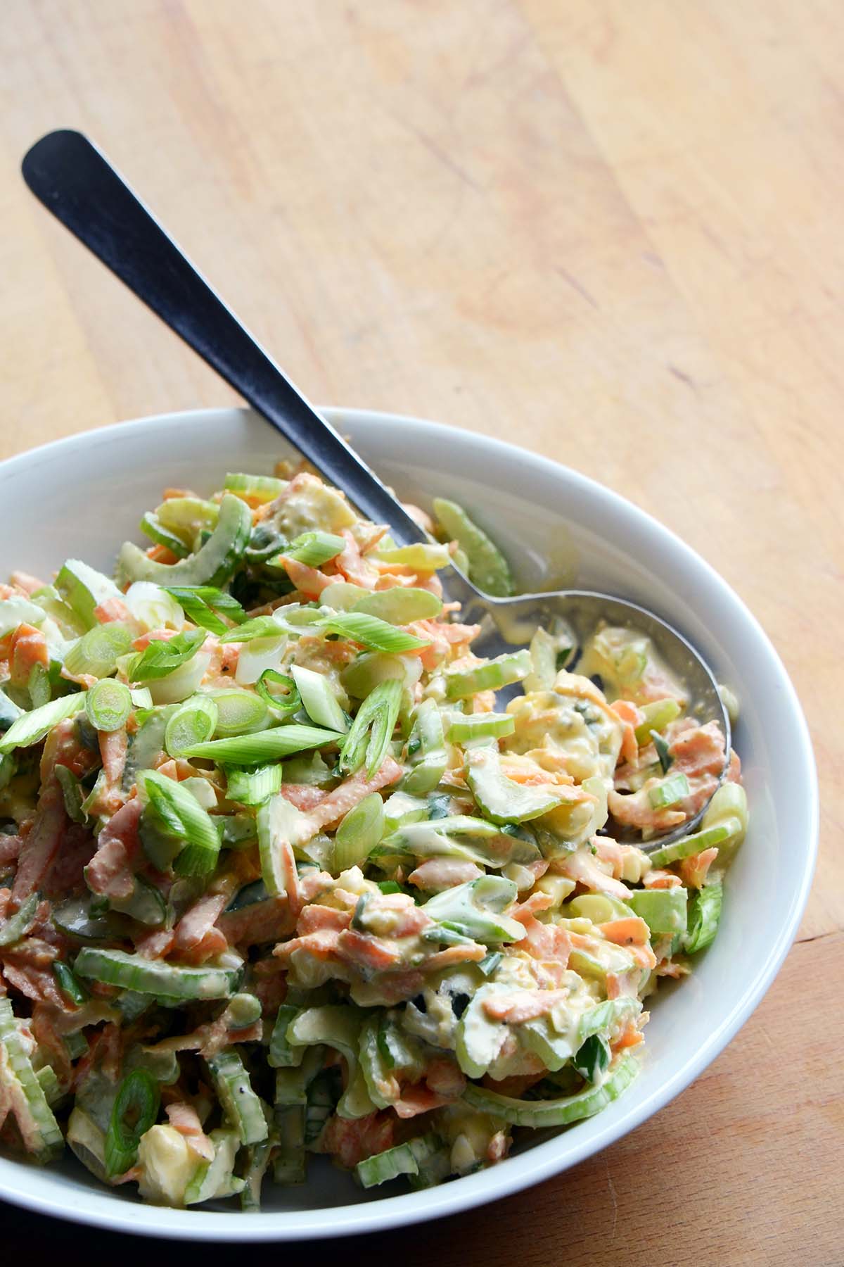 carrot and celery coleslaw in white bowl on wooden table