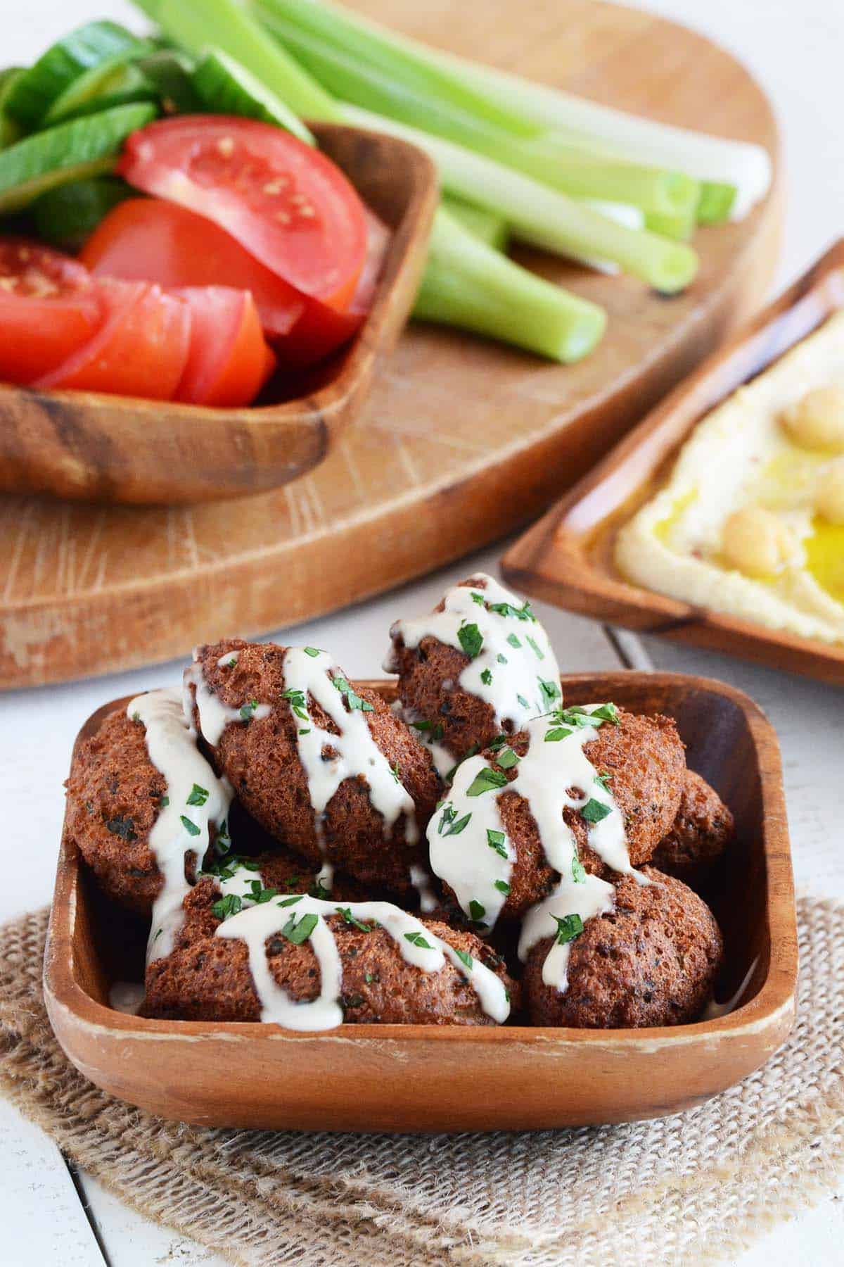 falafel fritters topped with tahini sauce in wooden dish from an edible mosaic cookbook