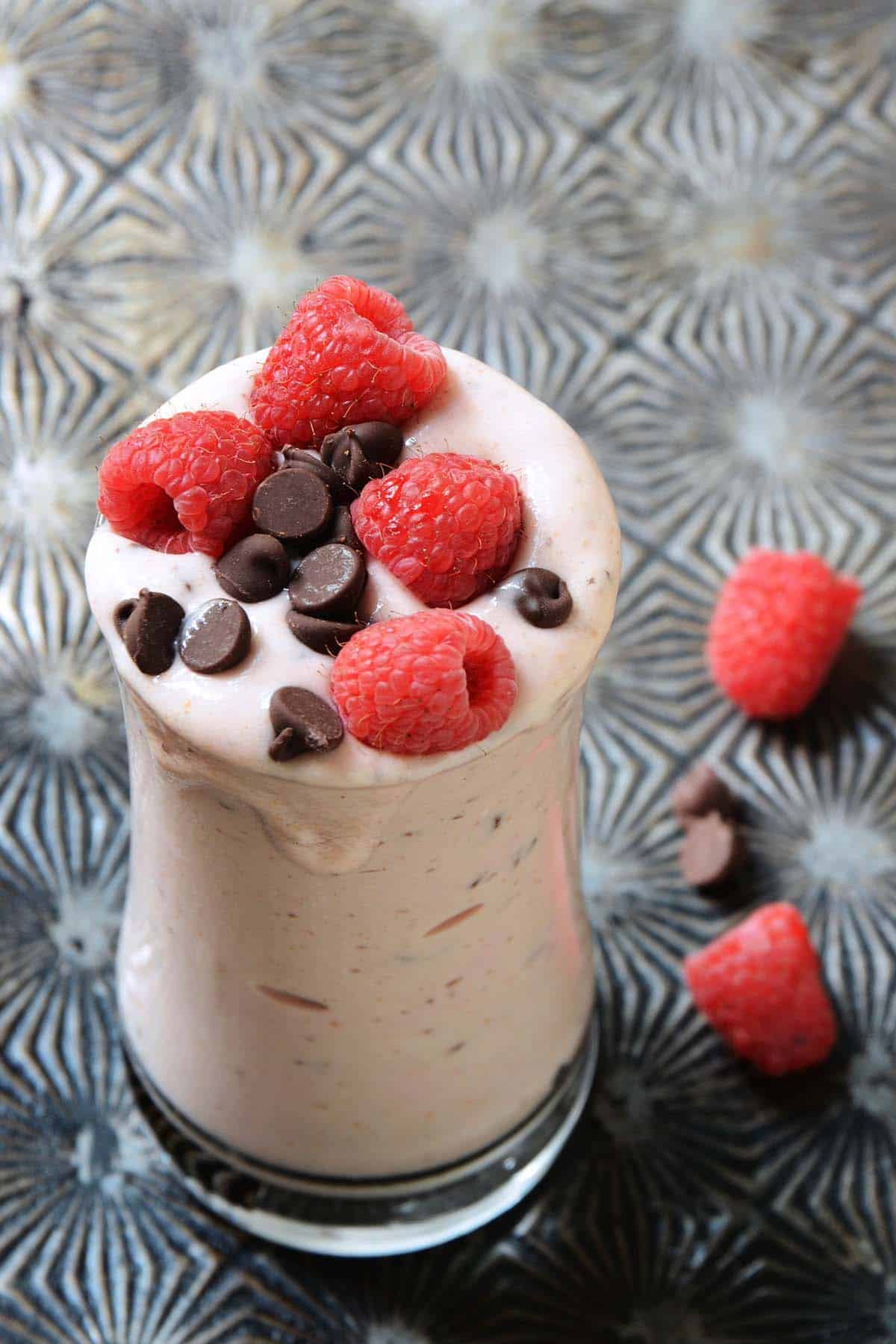 front view of cheesecake milkshake recipe in glass topped with berries and chocolate chips