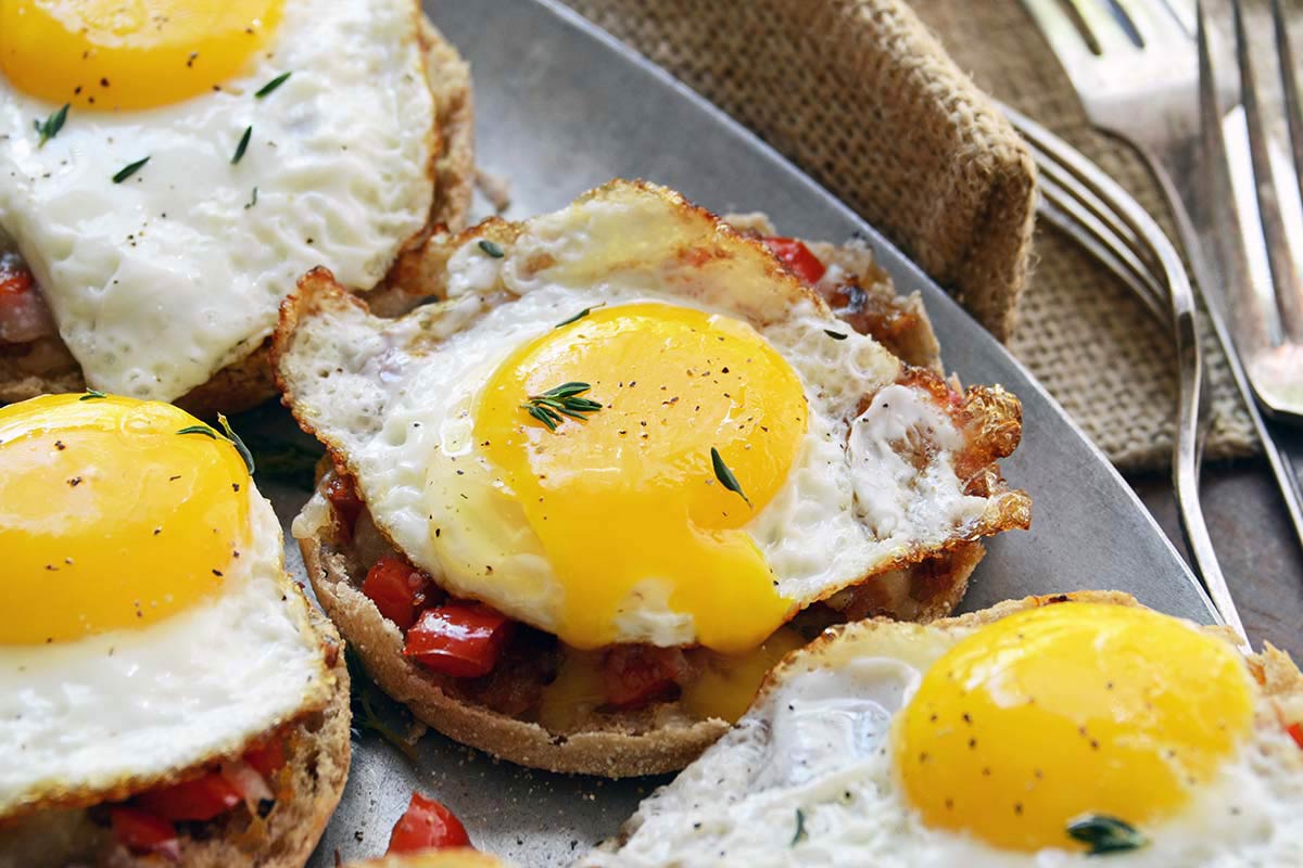close up of runny egg yolk on English muffin with cheese