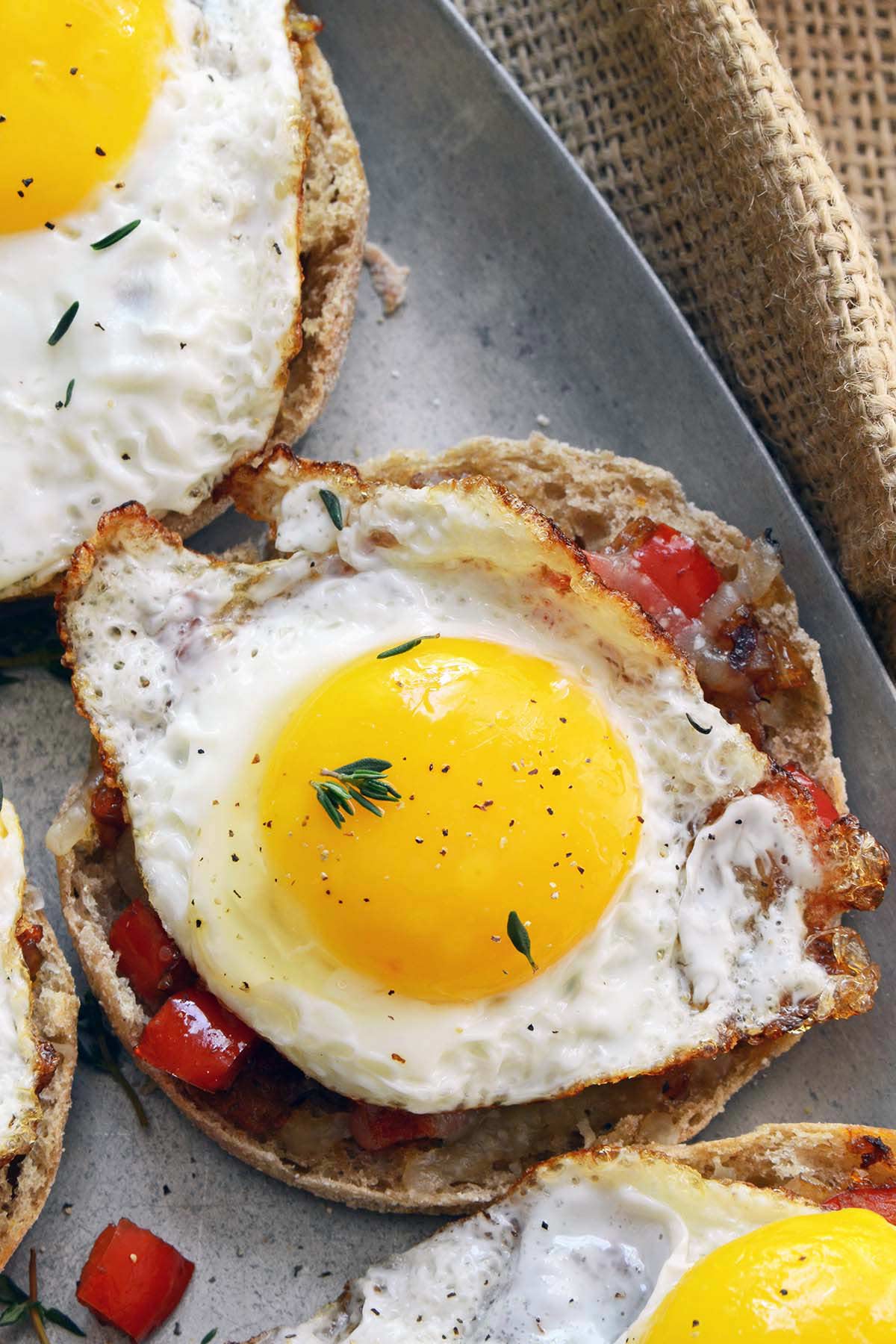 close up top view of half fried egg on top of cheesy English muffin with smoky bell pepper compote