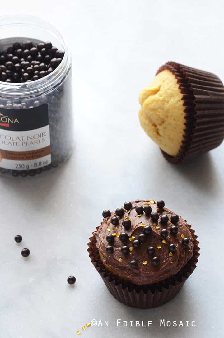 Yellow Cupcakes with Chocolate Frosting and Dark Chocolate Pearls on White Marble Countertop