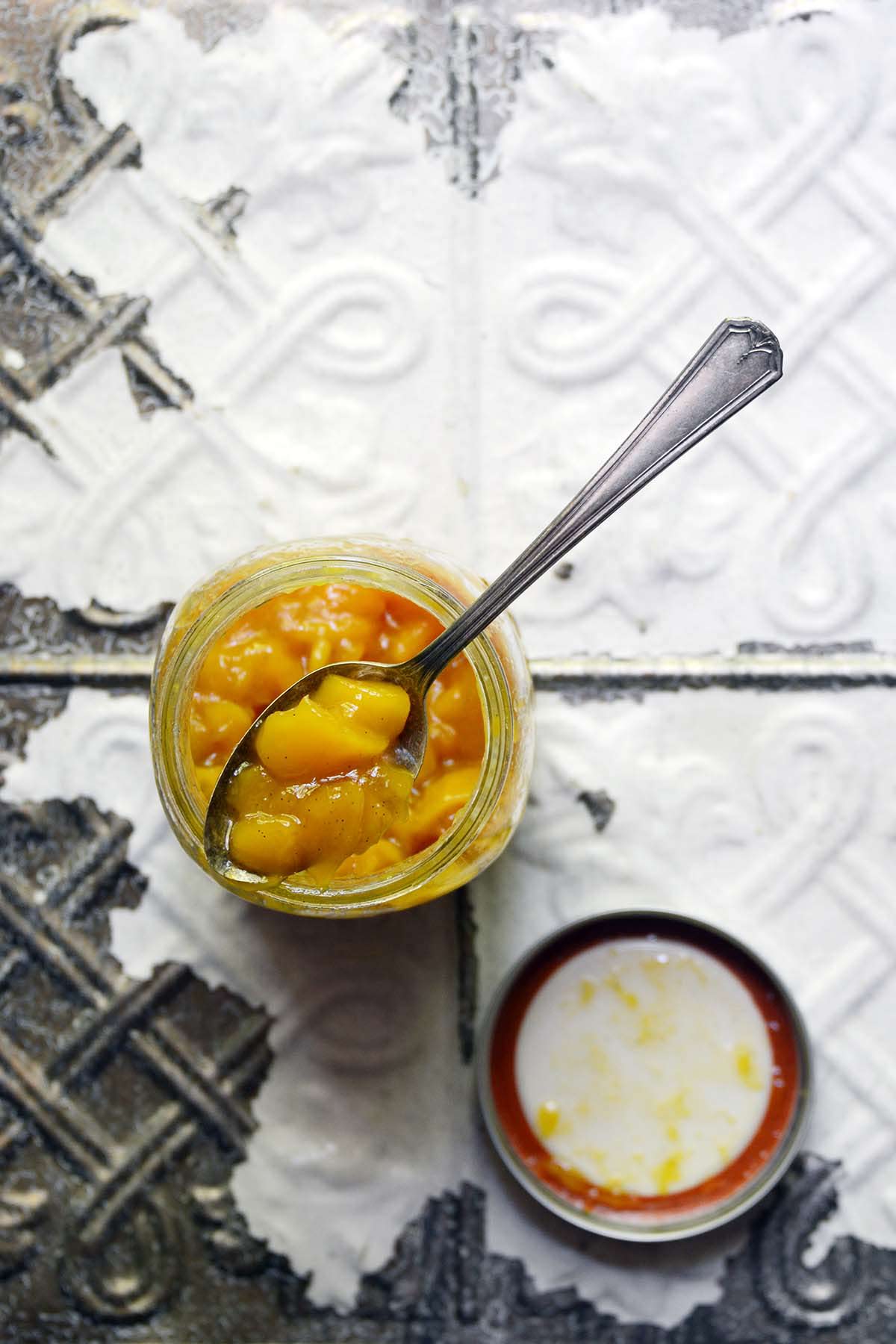glass jar of vanilla mango jam on chippy white vintage tile