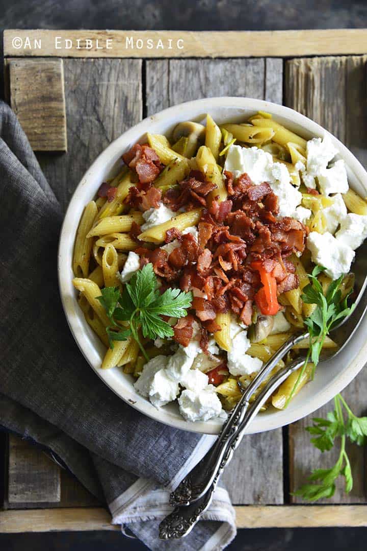 Warm Caramelized Leek Pasta Salad with Bacon and Goat Cheese on Wooden Background Top View