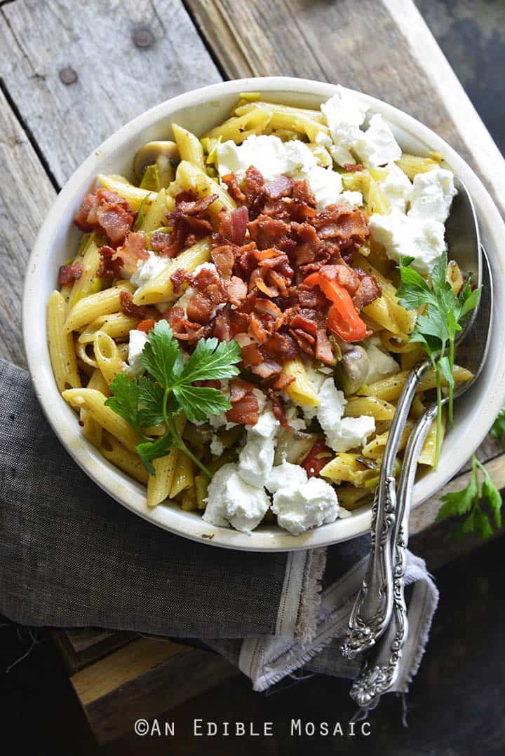 Warm Caramelized Leek Pasta Salad with Bacon and Goat Cheese on Wooden Background Front View