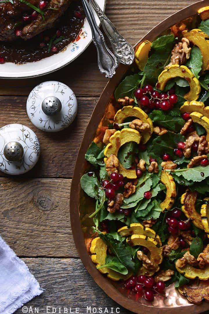 Roasted Winter Squash Salad with Spiced Walnuts, Red Currants, and Pomegranate Balsamic Vinaigrette with Cornish Hens and Decorative Salt and Pepper Shakers on Wooden Table