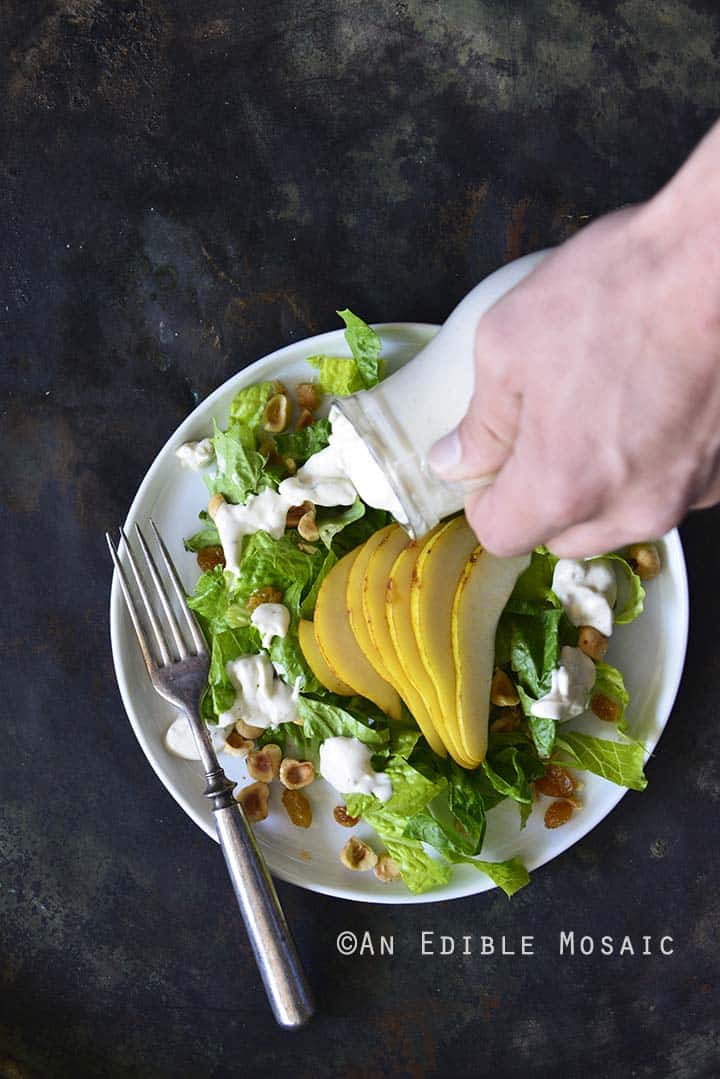 Pouring The Best Creamy Blue Cheese Dressing on Pear Hazelnut Salad