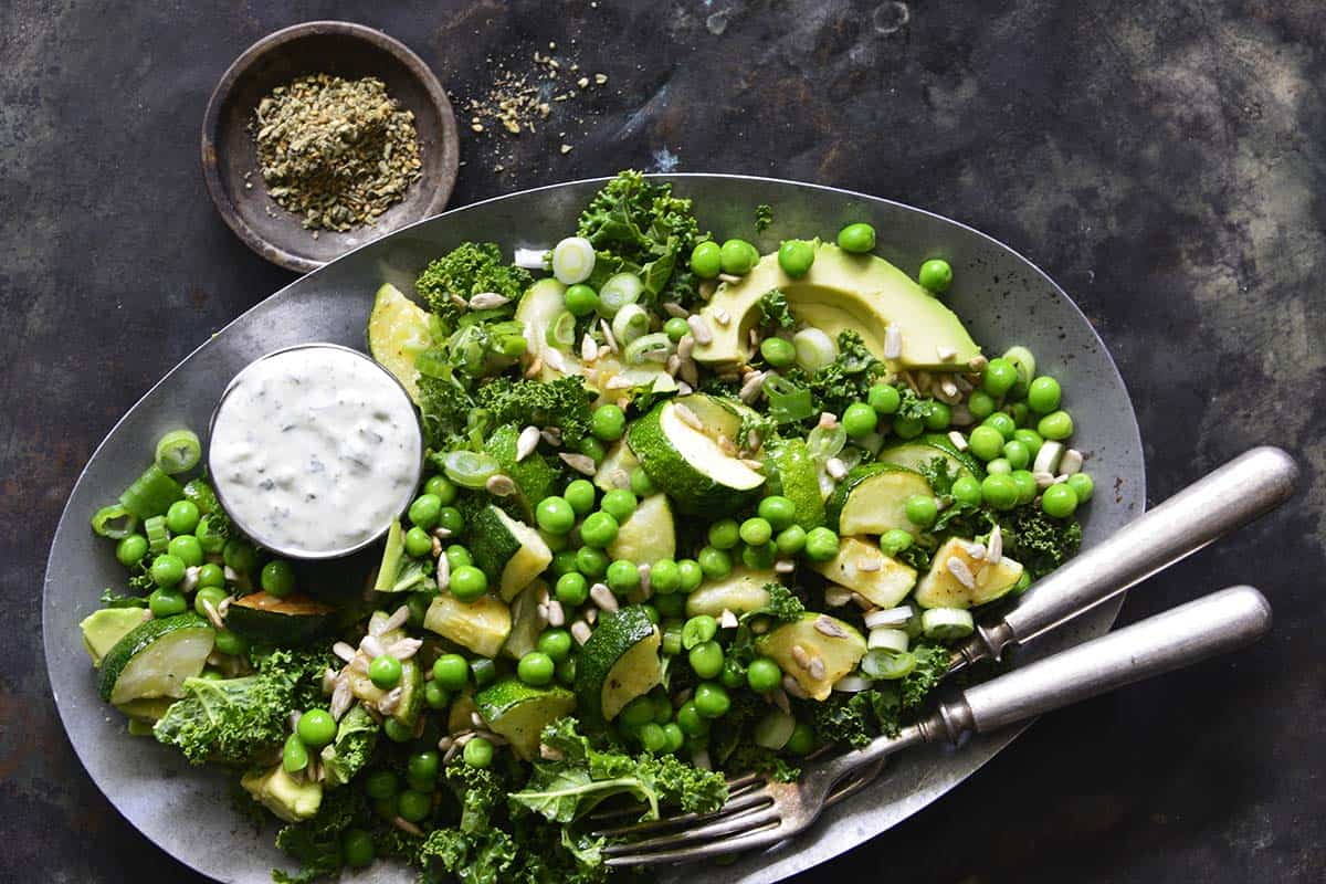 close up top view of platter of green salad with roasted vegetables and green peas