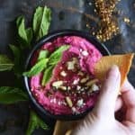 Hand Dipping Tortilla Chip Into Beet Hummus