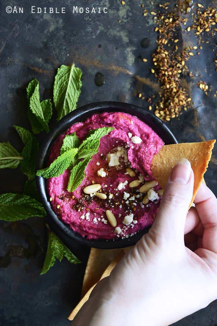 Hand Dipping Tortilla Chip Into Beet Hummus