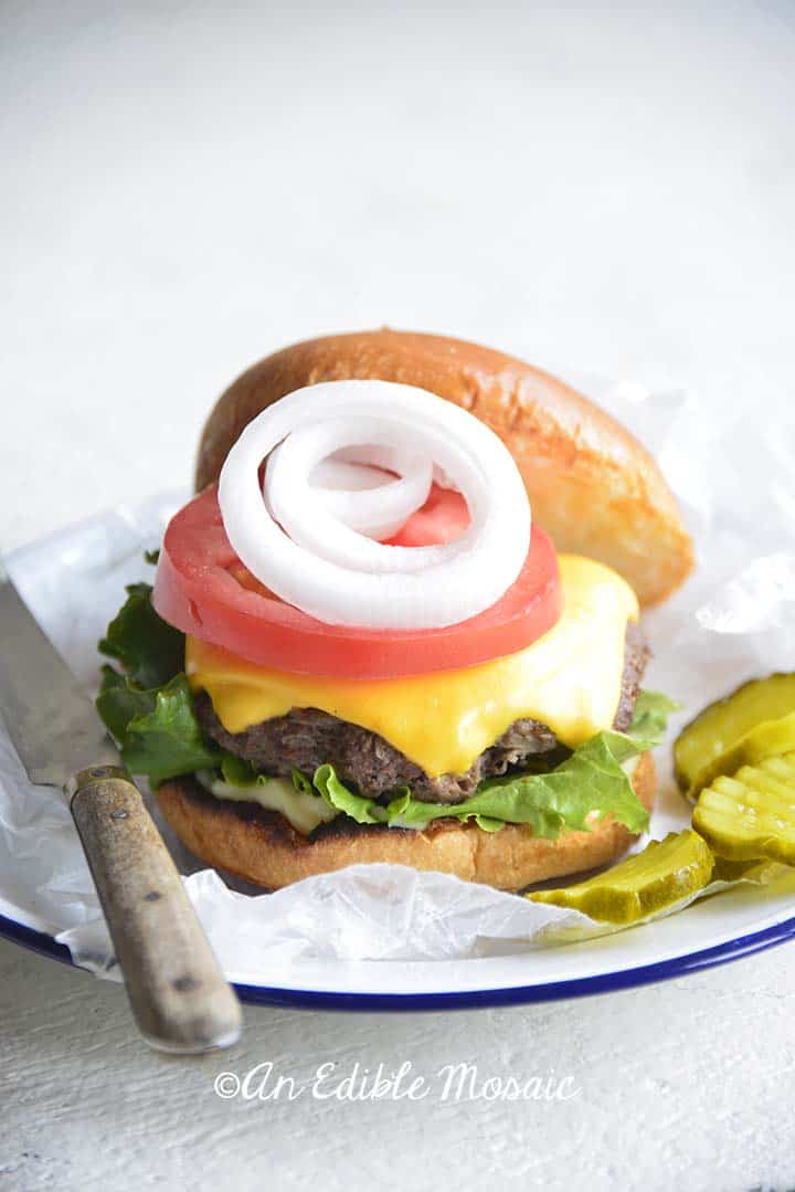 Front View of Cast Iron Burger on Bun with Lettuce Tomato Onion and Pickles on White Plate with Blue Rim