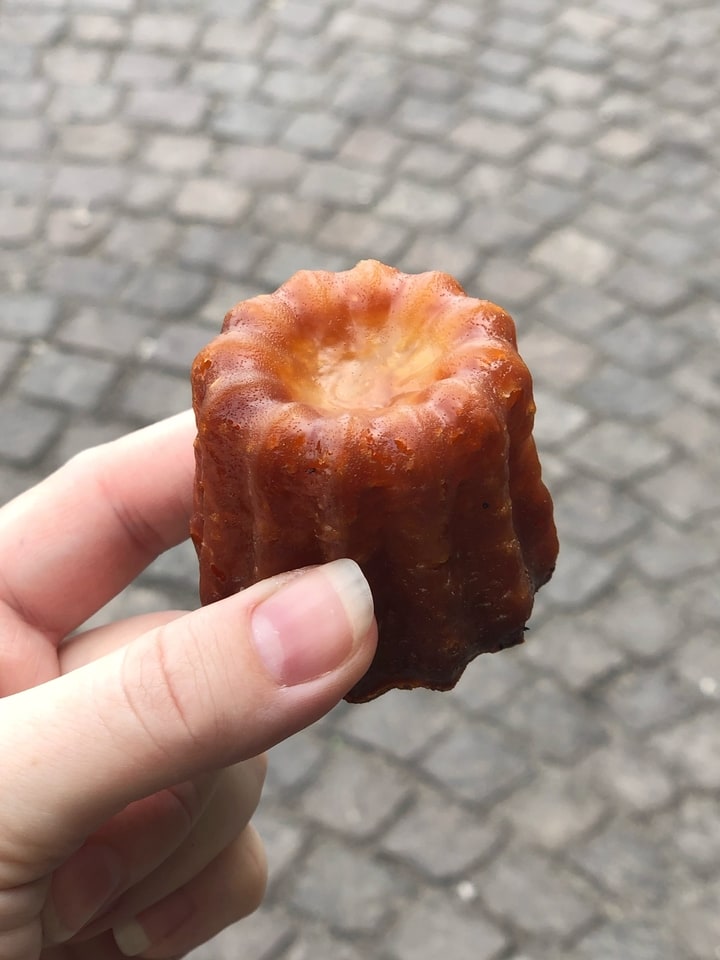 Hand Holding Canele over Cobblestone Road