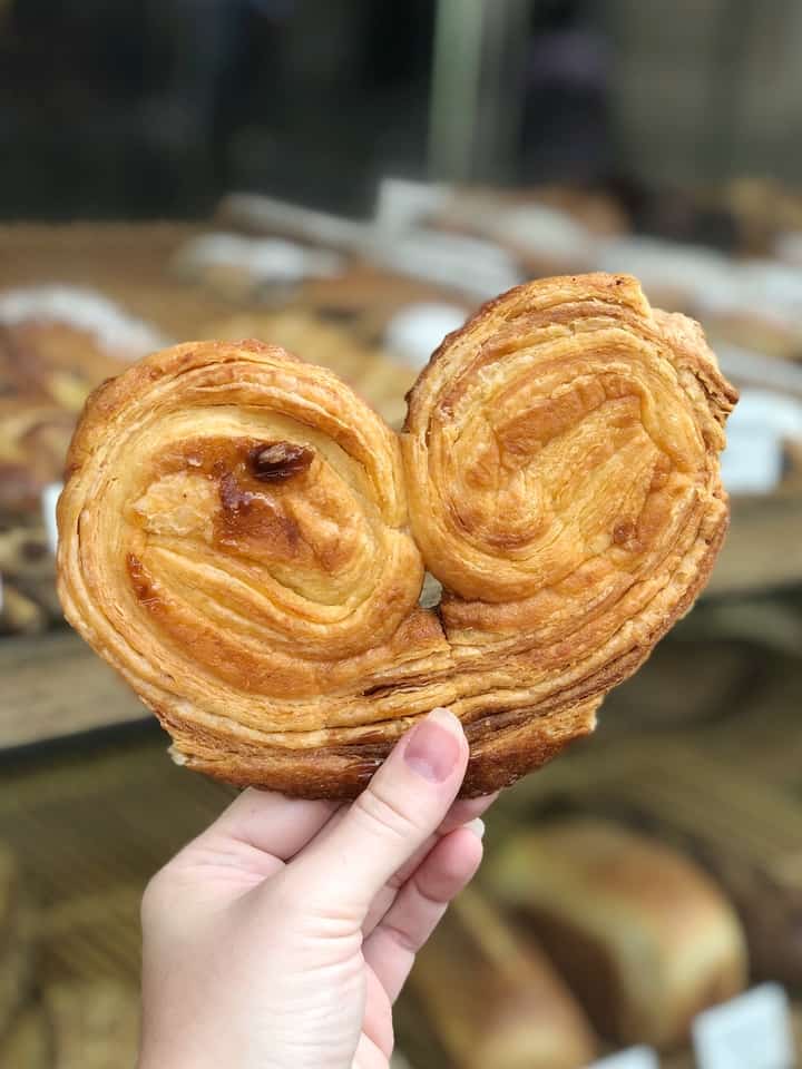 Hand Holding Palmier in Front of Bakery Window