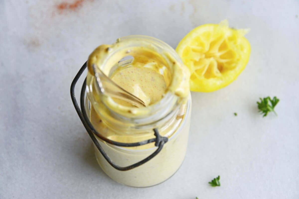 honey mustard salad dressing in glass jar with lemon rind behind