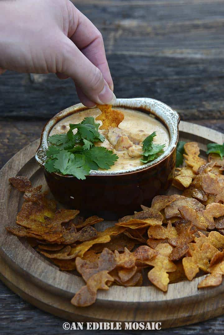 Hand Dipping Into Pumpkin Queso Dip with Spooky Dipper