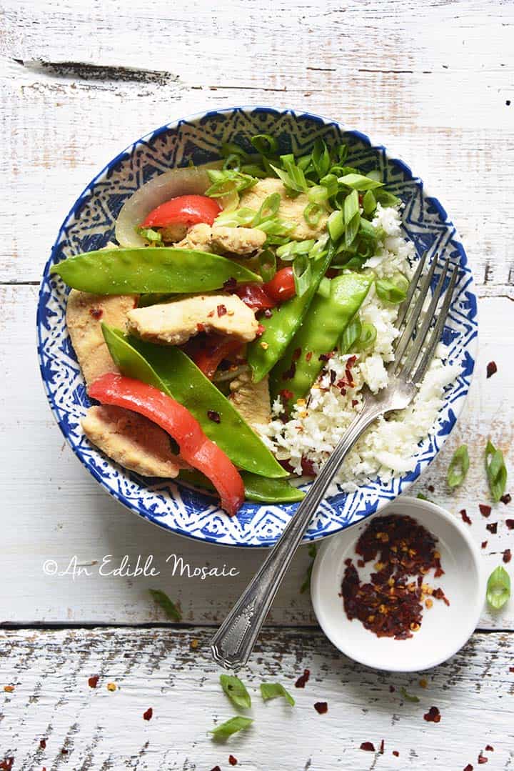 Overhead View of Healthy Sweet and Sour Chicken Stir Fry with Small Dish of Crushed Red Pepper Flakes