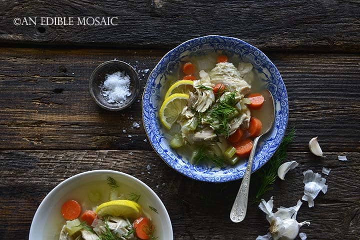Homemade Chicken Soup Recipe in Blue and White Bowl with Vintage Spoon and Garlic Peels on Wood Table