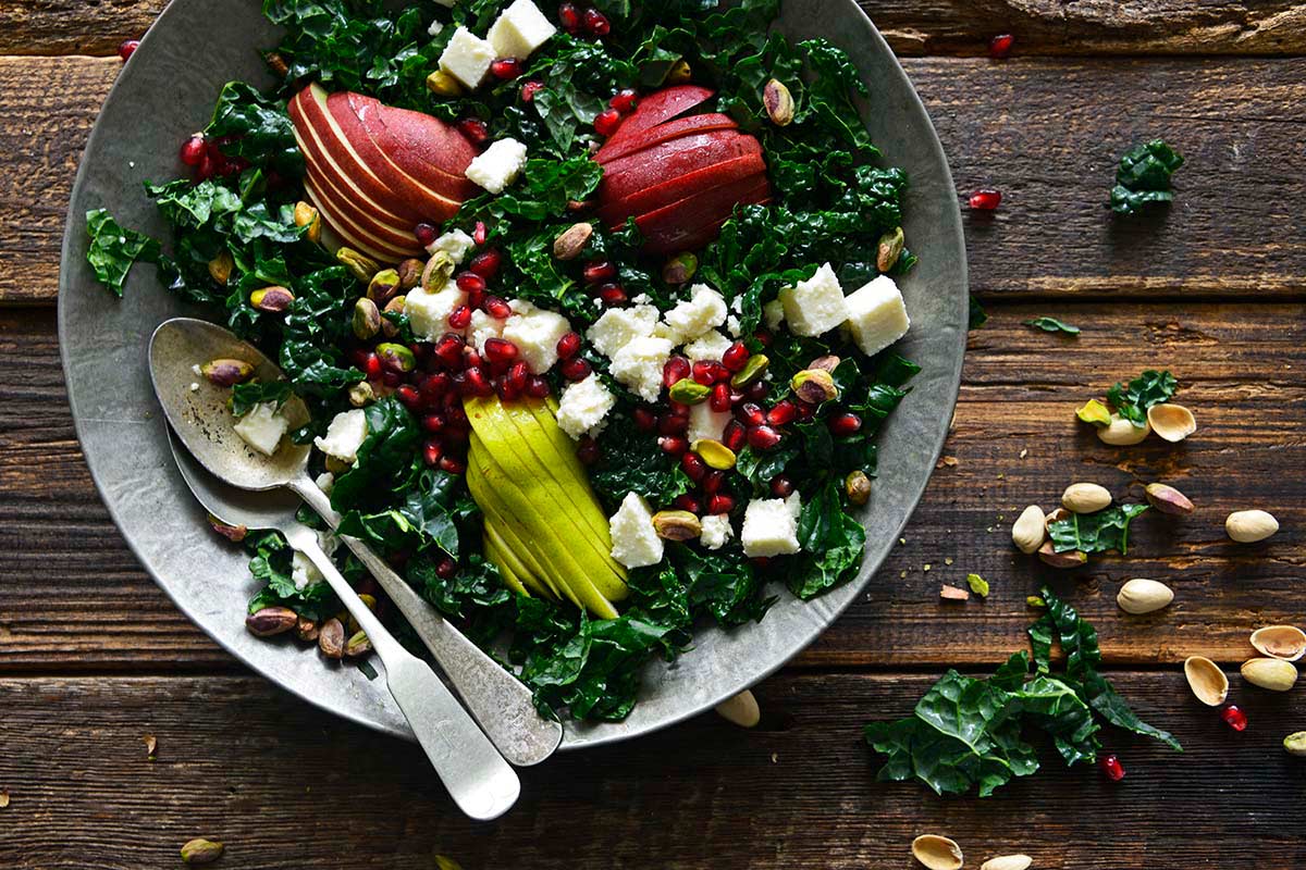 kale winter salad with pomegranate on rustic wooden table