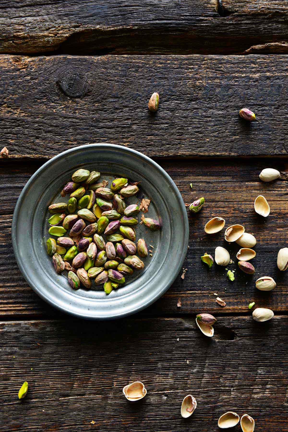 silver dish with pistachios with shells around on wooden table