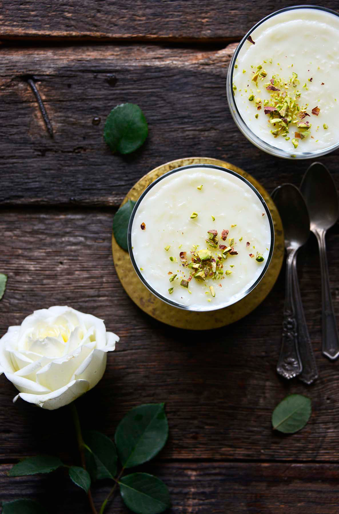 top view of Syrian creamy rice pudding in serving glasses on dark wooden table with white rose