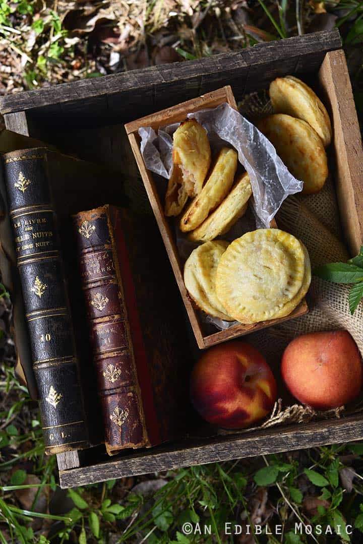 Peach Hand Pies with Fresh Peaches and Vintage Books in Wooden Crate Outside on Grass