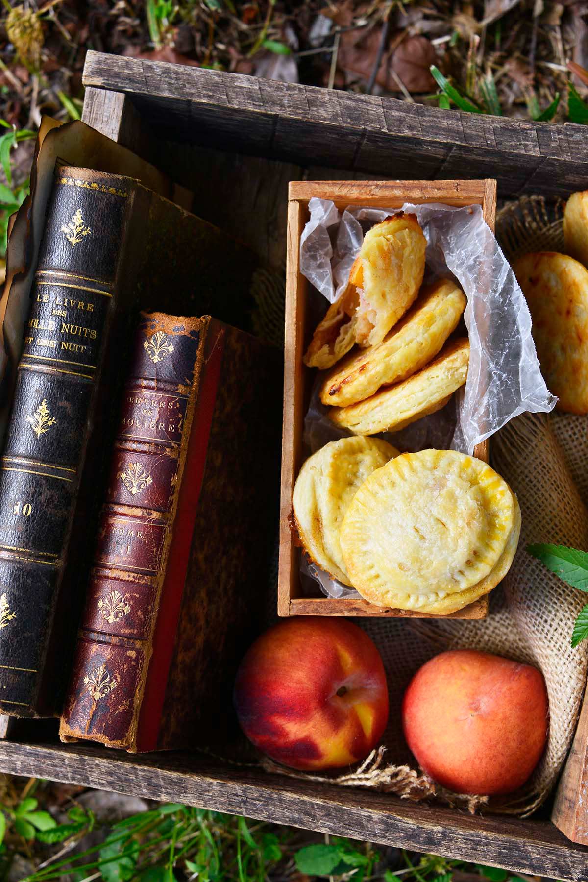 fresh peach hand pies in wooden box with books on lawn