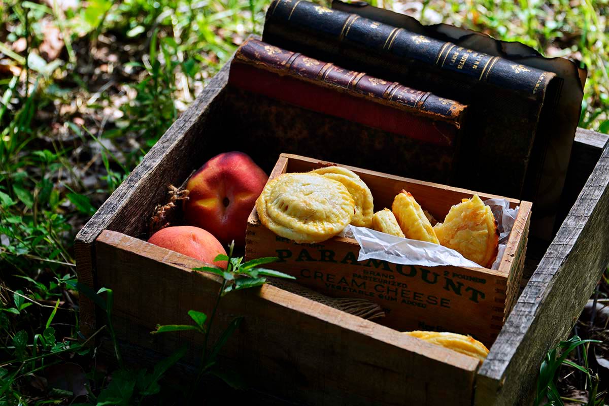 wooden picnic box with fresh peaches hand pies and books on grass