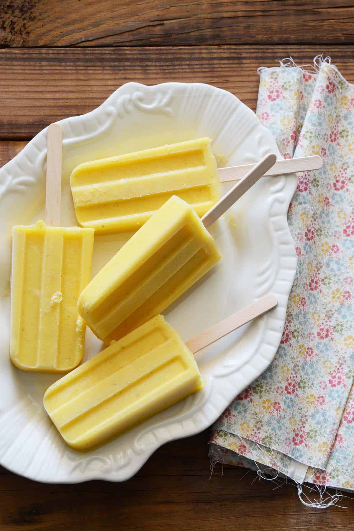 overhead view of easy homemade pineapple popsicles on white tray with floral towel