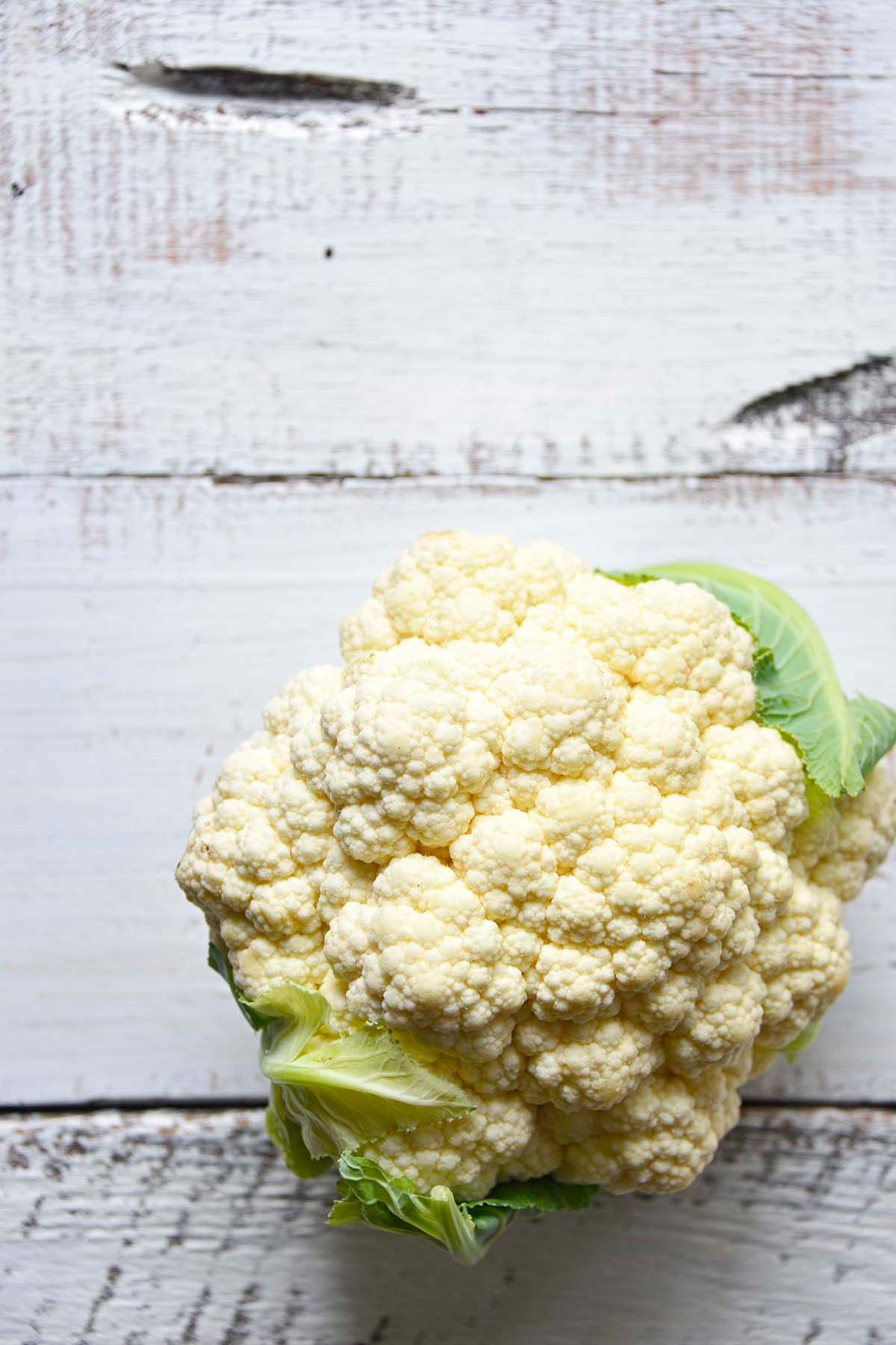 whole head of cauliflower on wooden white farmhouse table