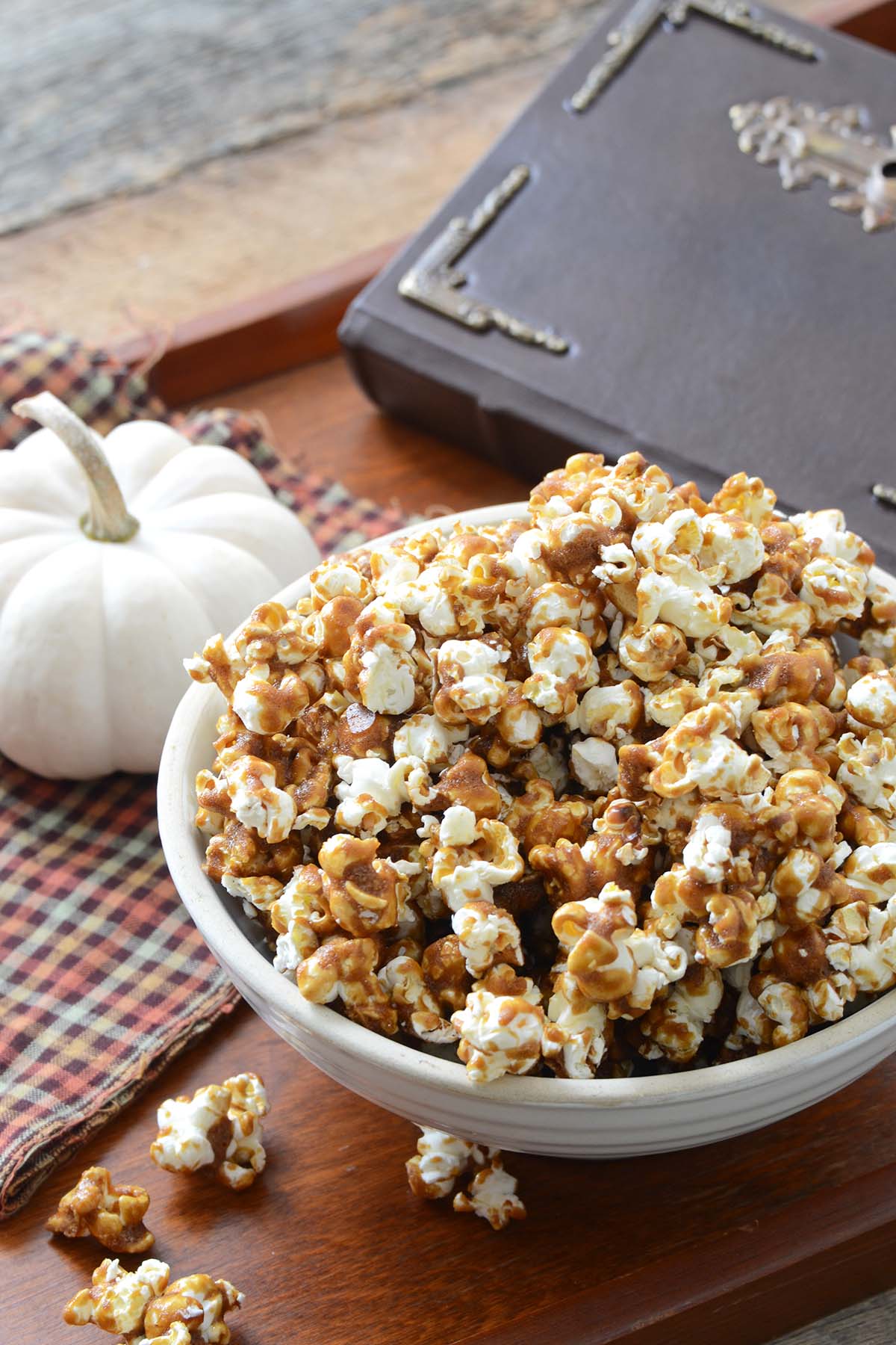 butterbeer popcorn in white bowl on wooden tray with small white pumpkin