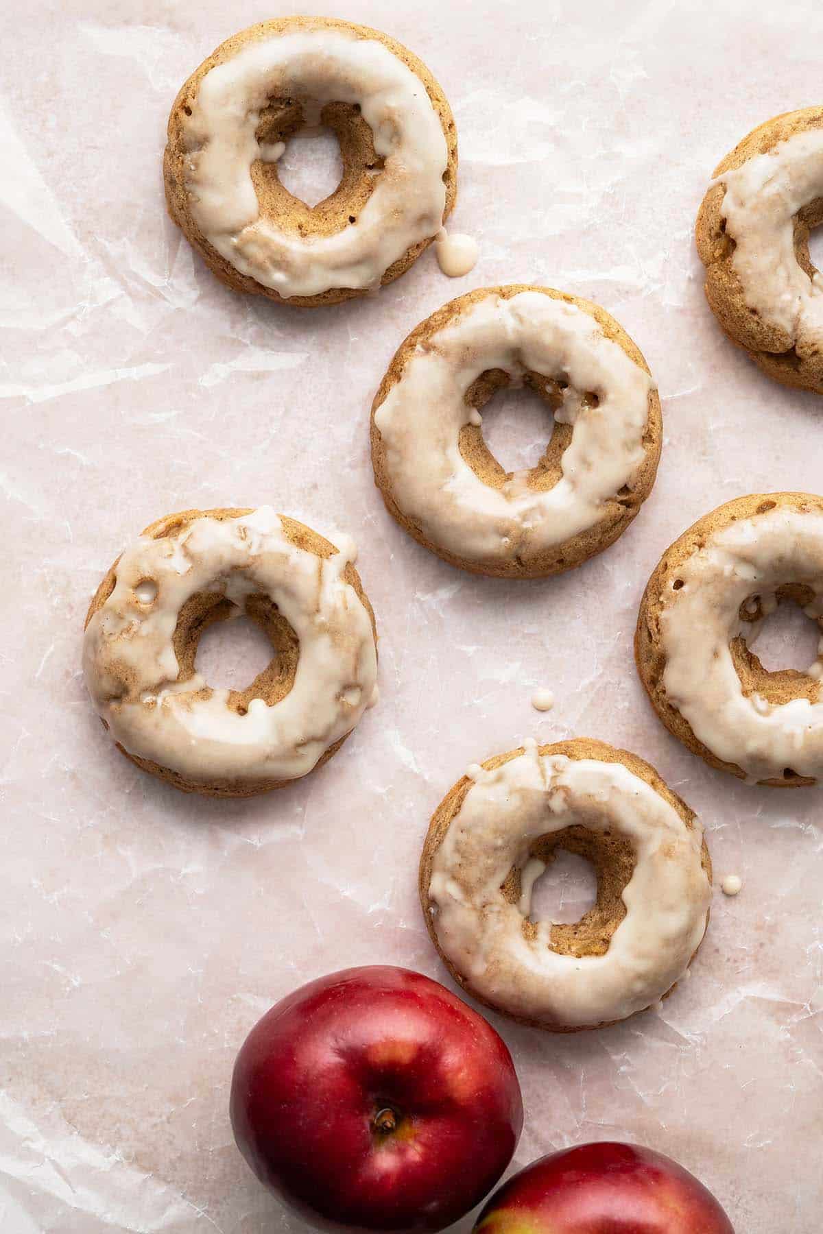 overhead view of baked apple cider donuts dipped in glaze on parchment paper