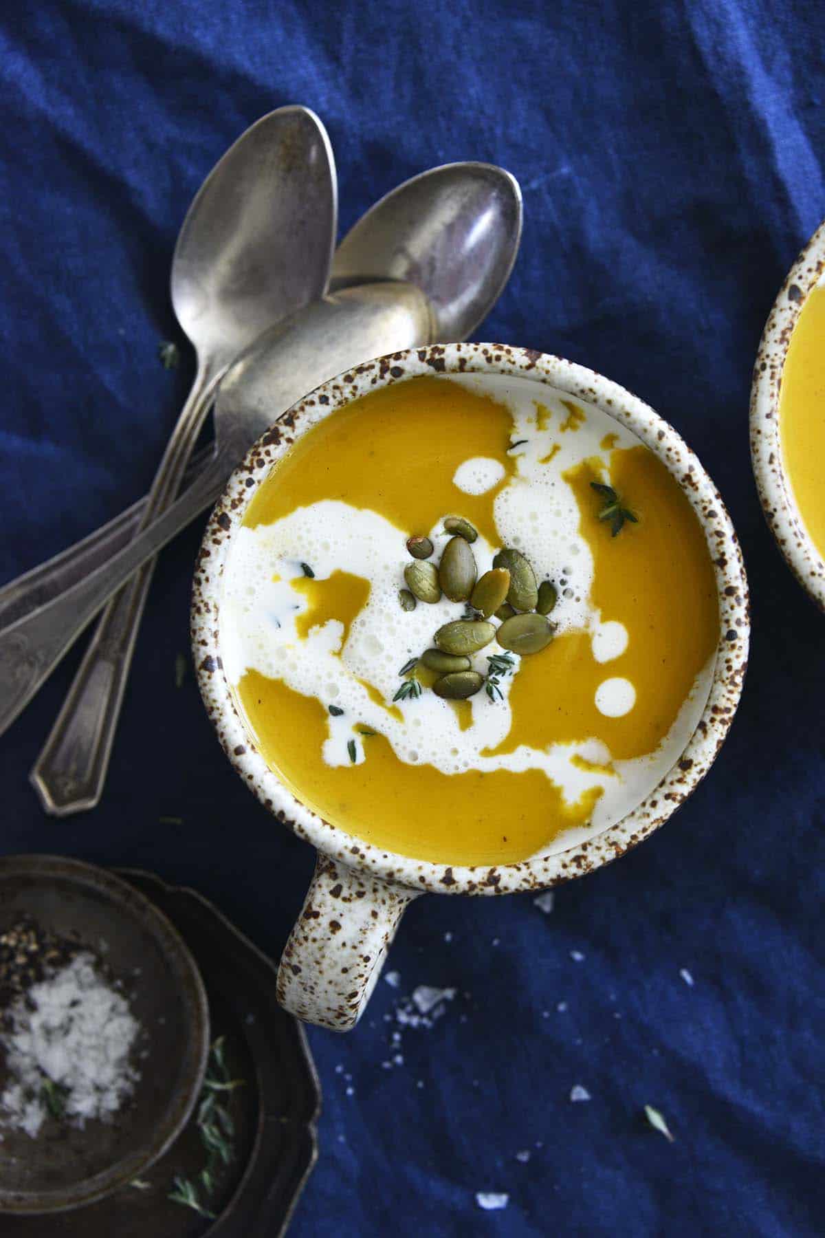 top view of squash soup in cup on blue fabric tablecloth