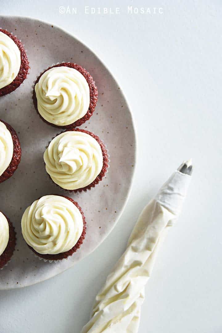 Piping Cream Cheese Frosting on Red Velvet Cupcakes