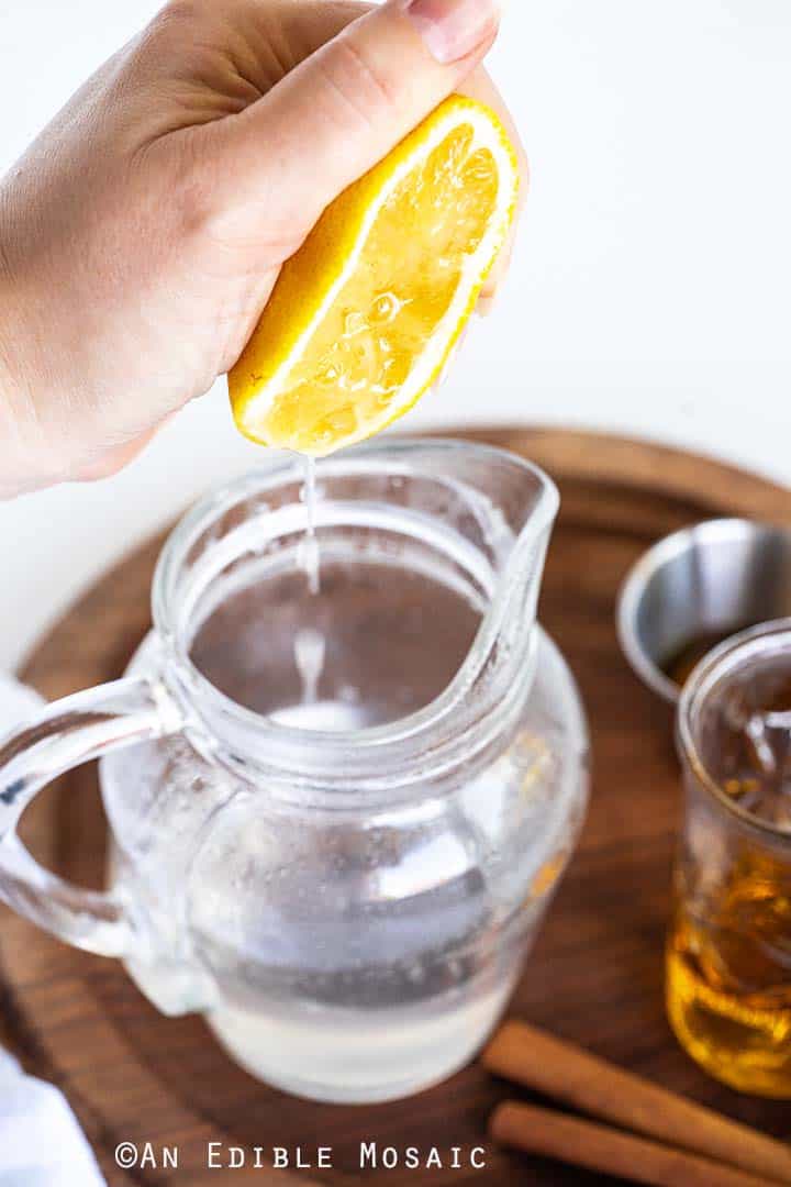 Squeezing Lemon Into Glass Pitcher with Water