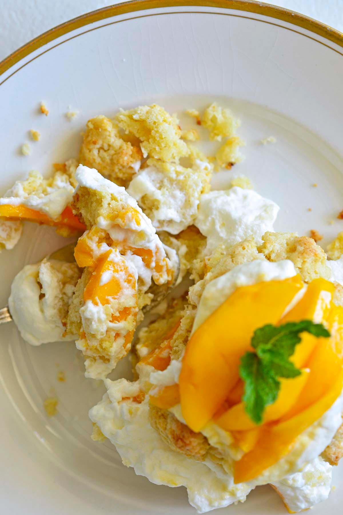 partially eaten mango short cake dessert on gold rimmed white plate