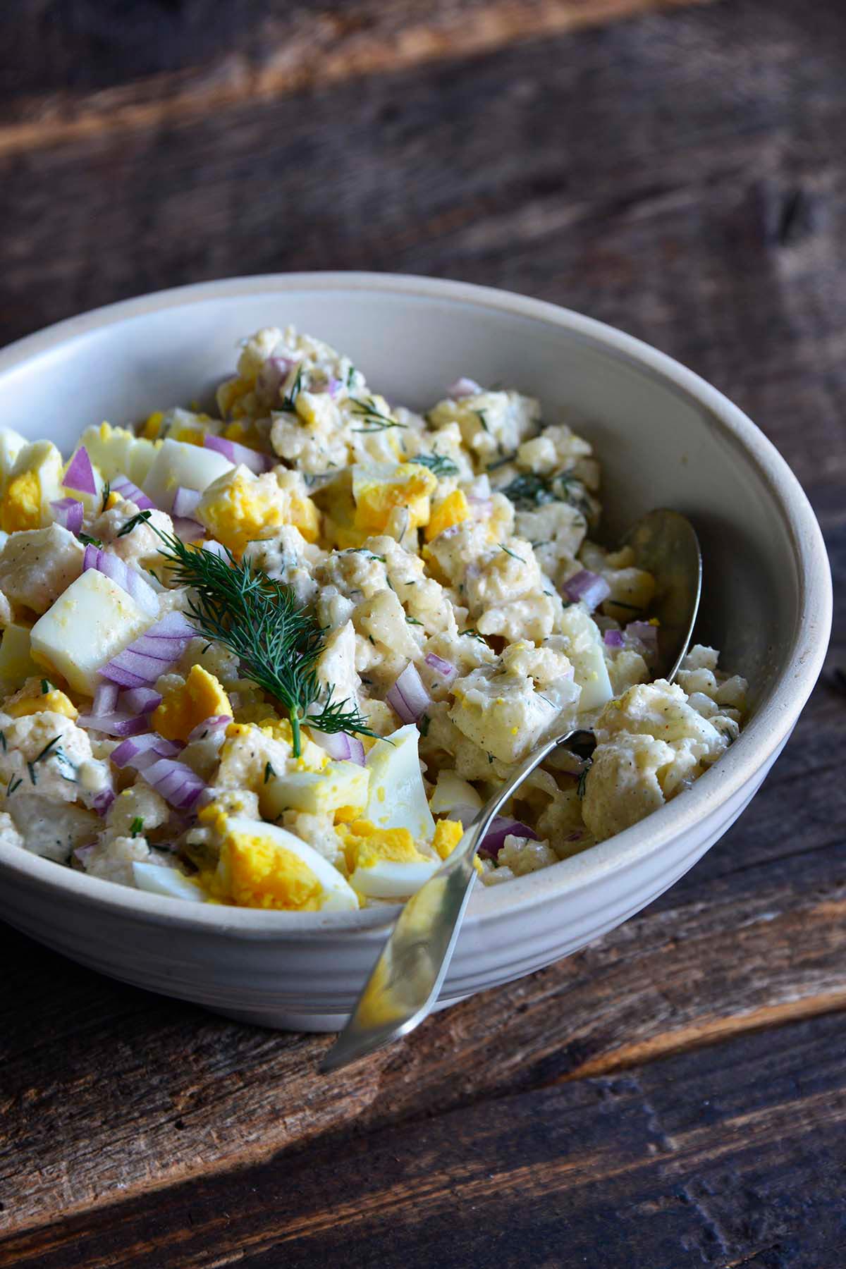 front view of cauliflower potato salad for low carb picnic side dish in stoneware bowl