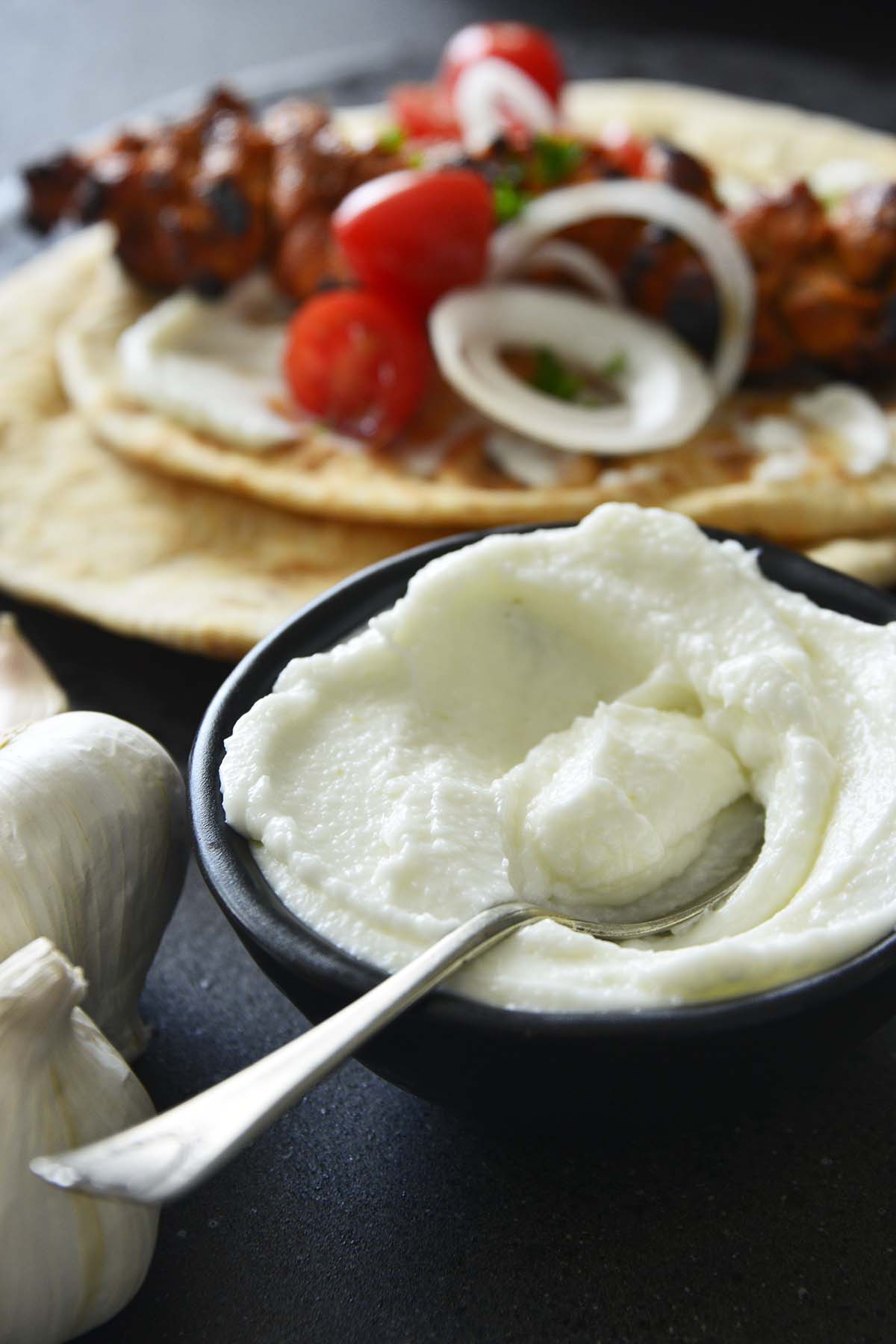 bowl of middle eastern garlic dip with shish tawook in background