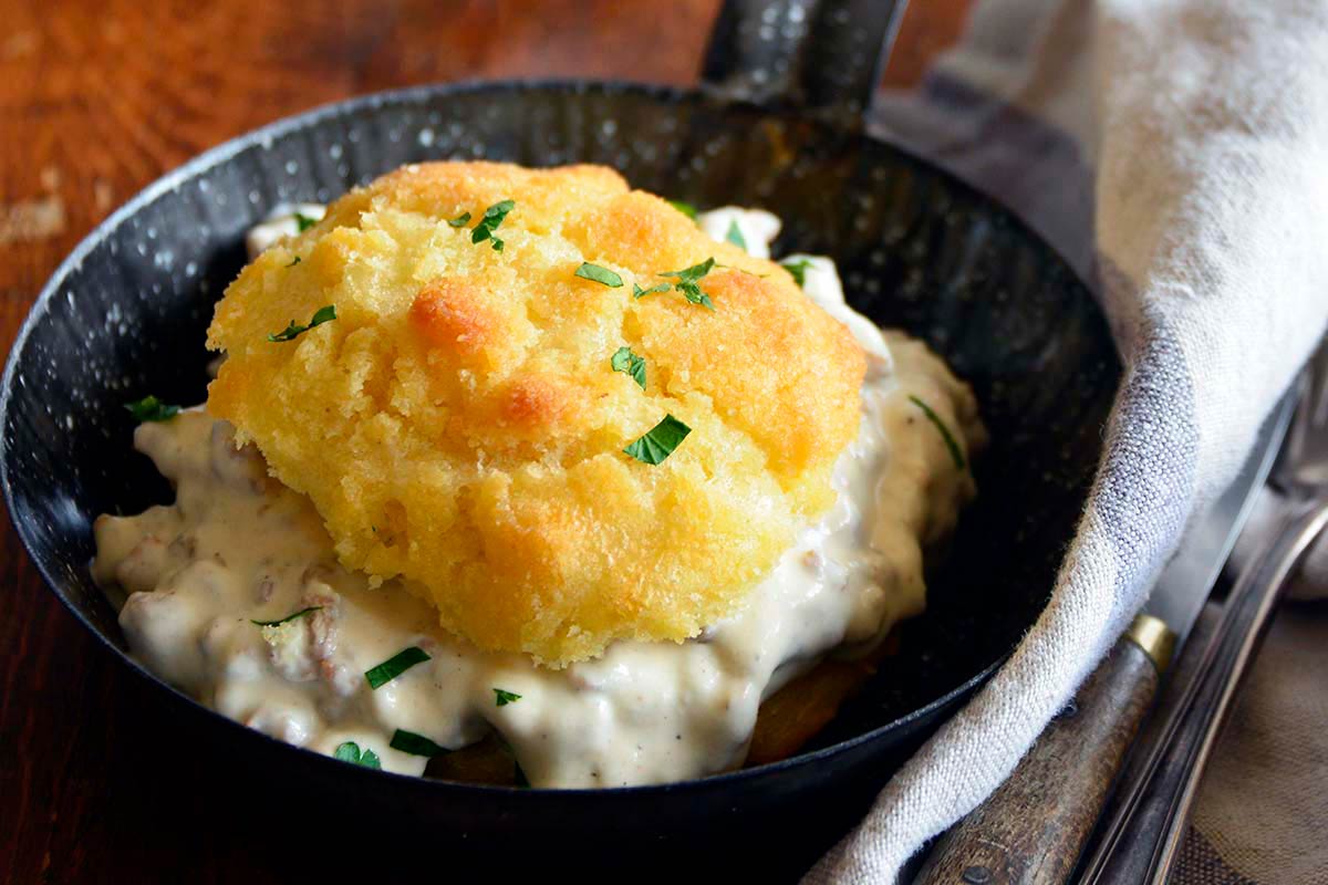 close up of keto biscuits with creamy white turkey sausage gravy in small enamelware skillet