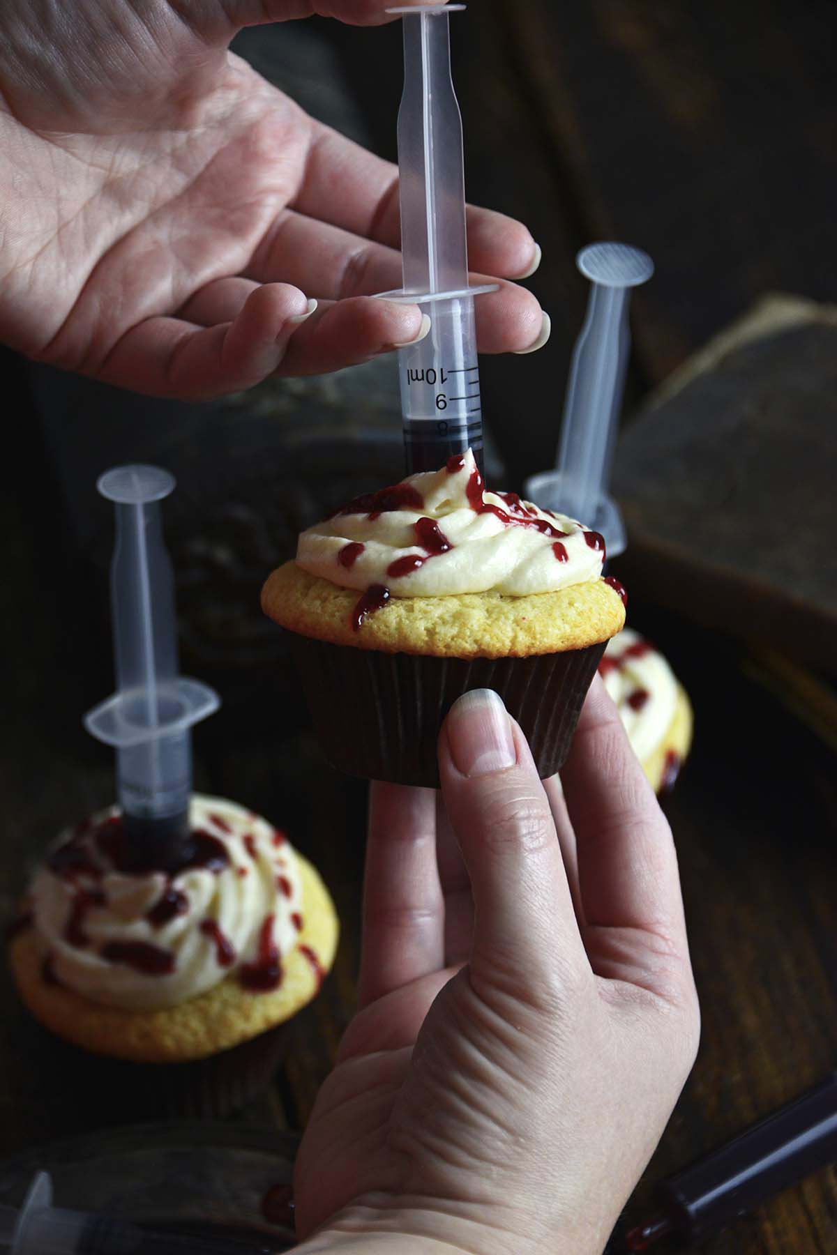 hands injecting bloody syringe into halloween cupcake