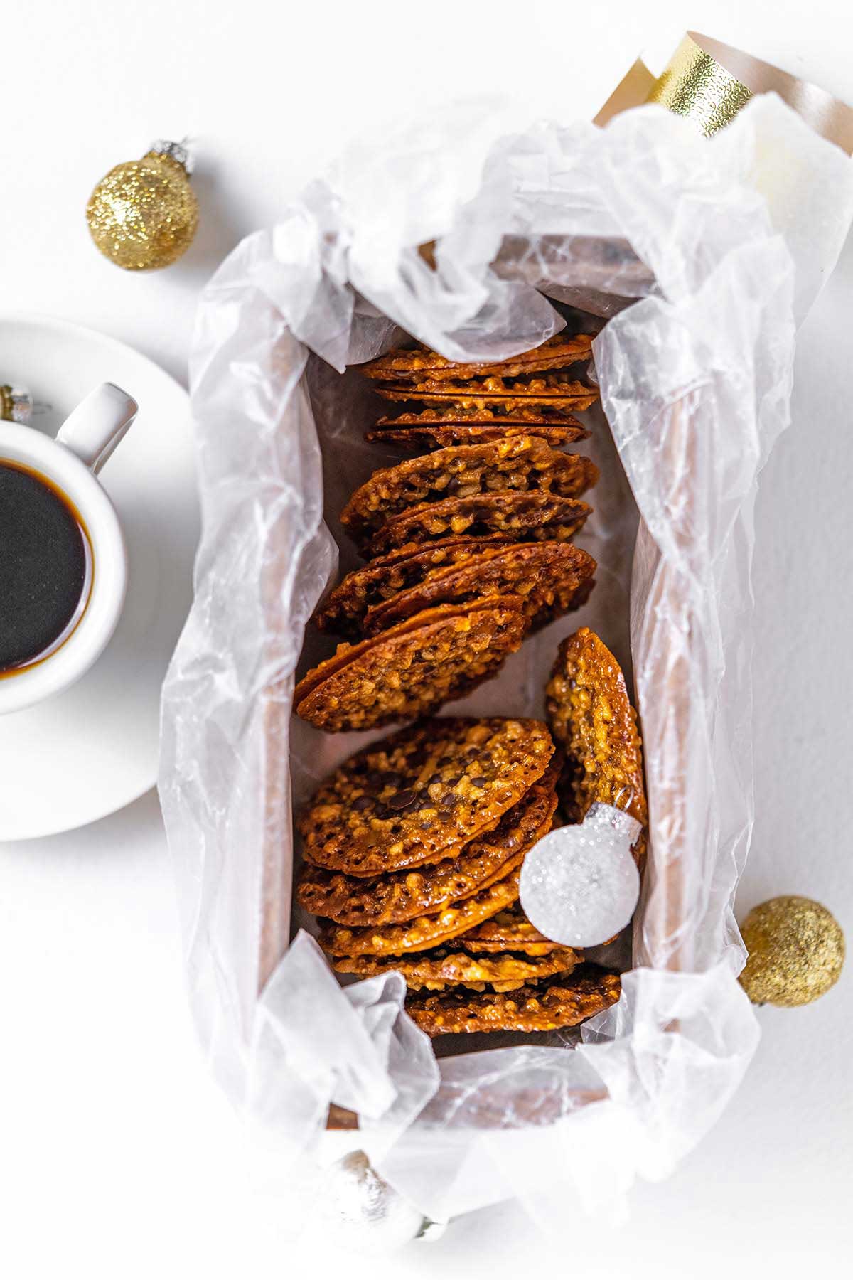 top view of pile of lacy nutty caramel chocolate sandwich cookies with cup of coffee