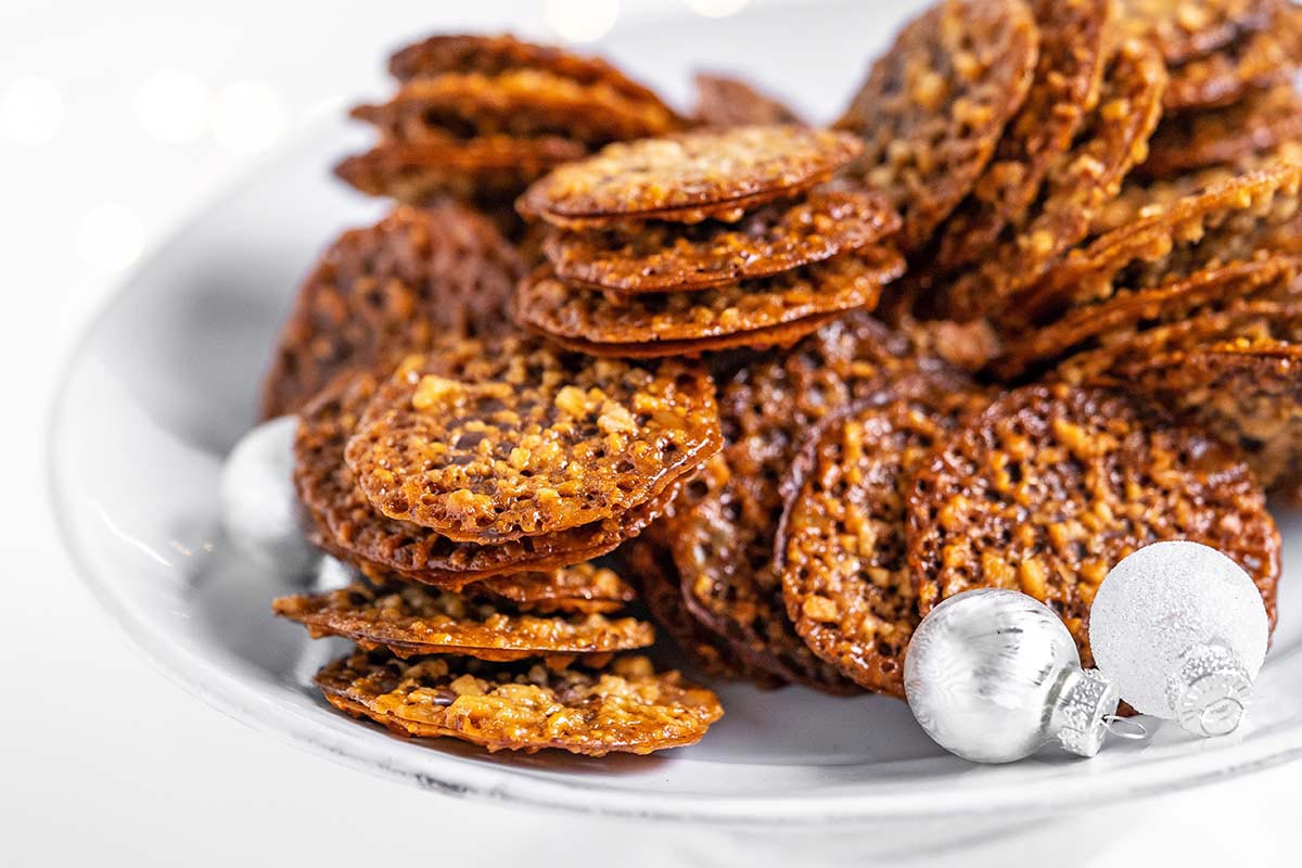 white platter with Florentine chocolate cookies with Christmas ornaments and twinkling lights in the background