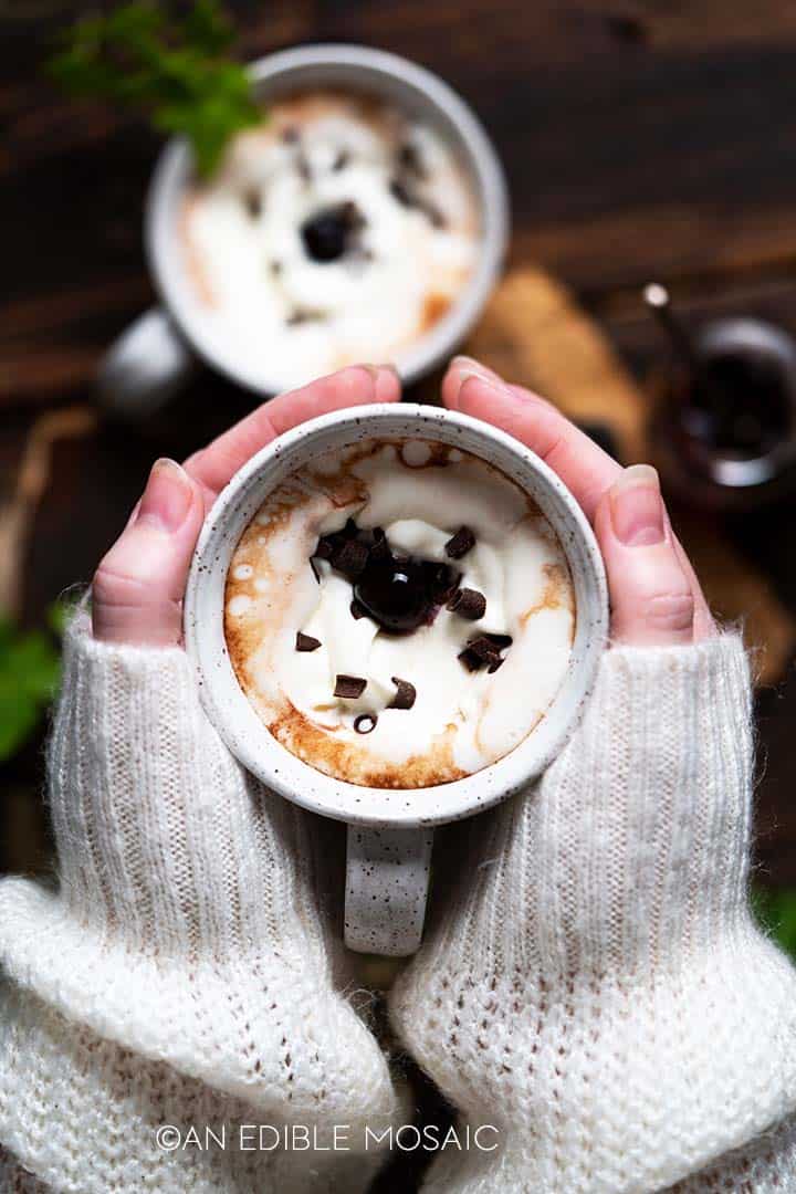 hands holding ceramic mug of hot chocolate with cozy sweater