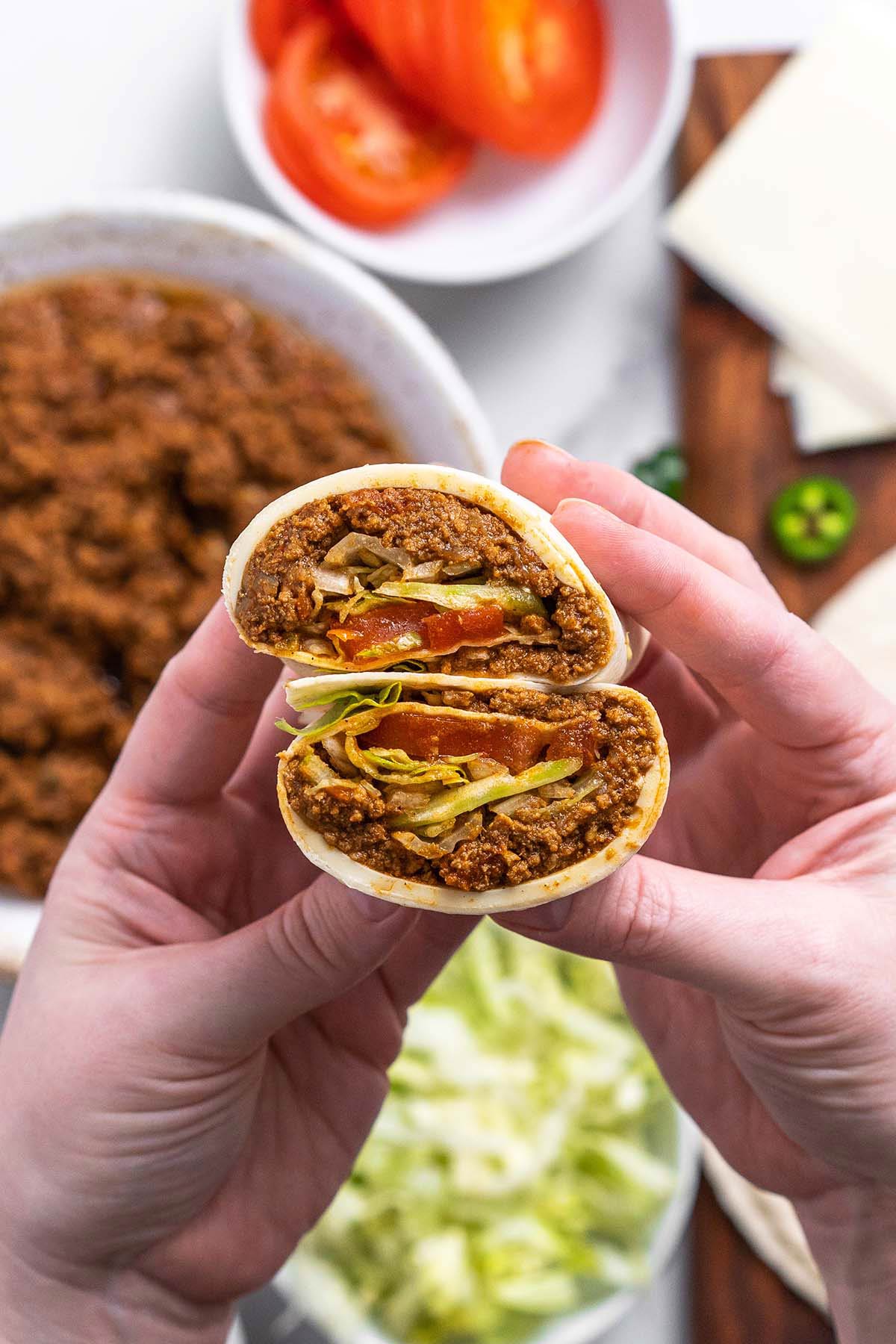 hands holding homemade mighty taco with seasoned beef and American Swiss cheese