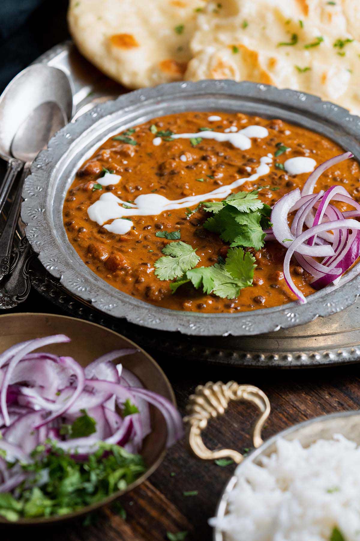 front view of daal makhani in dish with cilantro and red onion garnishes